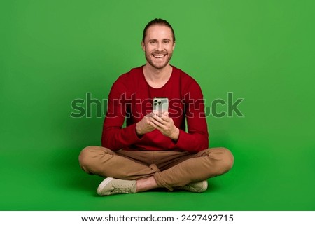 Full size photo pleasant guy wear red shirt brown trousers sit with smartphone read notification isolated on green color background