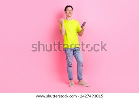 Full length photo of good mood dreamy guy wear green t-shirt typing modern device thumb empty space isolated pink color background