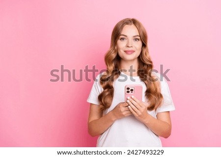 Portrait of positive gorgeous girl with curly hair dressed white t-shirt holding smartphone in hands isolated on pink color background