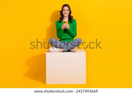 Full body size photo of young girl wearing green jumper jeans sit with phone buy something online isolated on yellow color background