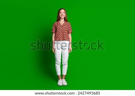 Full length photo of girlish positive cheerful girl dressed print shirt white pants smiling isolated on vivid green color background