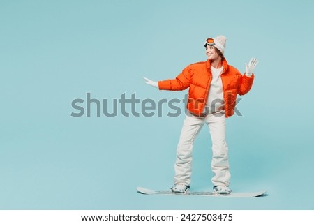 Full body confident young woman wear warm padded windbreaker jacket hat ski goggles mask snowboarding look aside travel rest spend weekend winter season in mountains isolated on plain blue background
