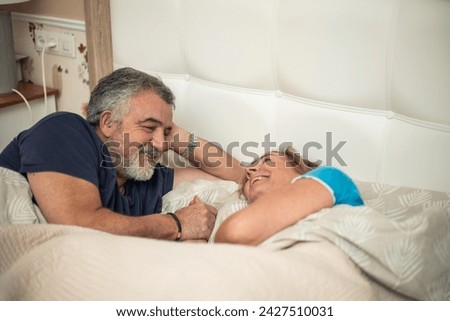 This touching image captures the essence of enduring love. A 60-year-old couple lies in bed, tenderly clasping hands and gazing at each other with deep affection. 
 Royalty-Free Stock Photo #2427510031