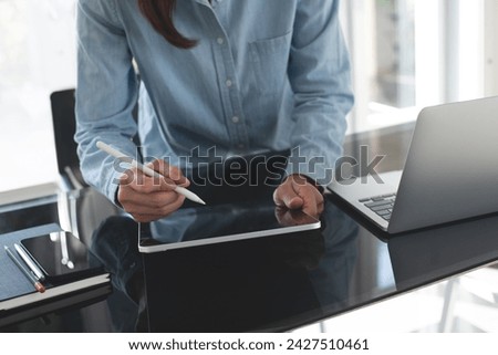Female designer working, using stylus pen and digital graphic tablet, laptop computer at studio office. Young casual business woman, freelancer standing at desk, online working at home office
