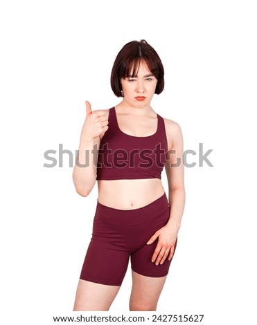 Annoyed young brunette fitness woman doing a thumb up gesture with closing one eye against a white background