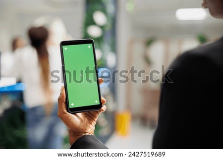 Woman holding mobile phone with green screen in hand while shopping in boutique. African american woman using smartphone with blank chroma key display in department store