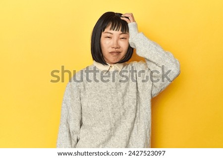 Young Chinese lady, yellow studio background tired and very sleepy keeping hand on head.