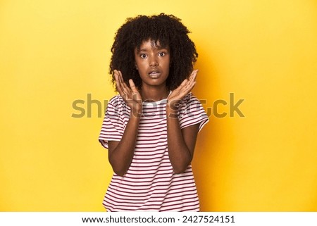 Teen girl in red striped T-shirt, yellow studio backdrop surprised and shocked.