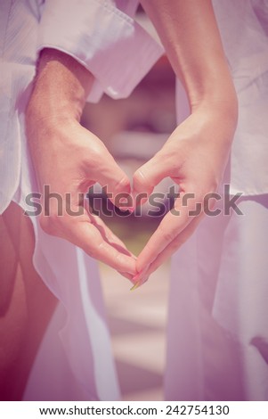 hands in the shape of a heart on the background of the sea  Male and female hands with rings