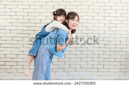 Happy asian beautiful young mother holding cute daughter little girl smiling posing on white brick wall background studio portrait Mother's Day love family parenthood childhood concept.