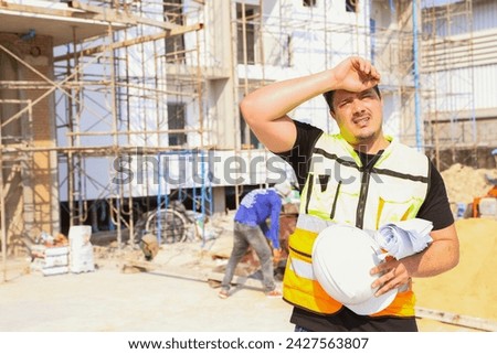 Foreman working outdoors condominium construction project exhausted from the hot weather and thirsty tired dizzy headache is dehydrated and wants to drink water suffer dehydration heatstroke. Royalty-Free Stock Photo #2427563807