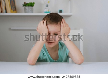 One sad, tired boy, holding his head while sitting at table in his room. Anxiety and stress. Concept of bullying, depressive stress or disappointment, sadness Royalty-Free Stock Photo #2427569835