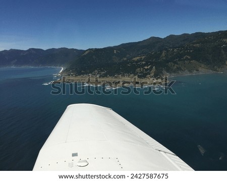 Coming into land at a small coastal airport.  The ocean surrounds the runway in this photograph taken from inside a small airplane with part of the wing in the picture.