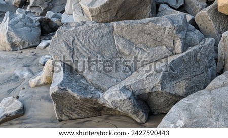 Granitic quarry rocks laid down along the shoreline for erosion control 50 years ago surrounded by polished river rocks all together at Swamis Reef Surf Park Encinitas California.