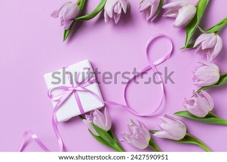 8 March. International Women's Day greeting card. Gift box and heap of fresh beautiful tulip flowers on pastel lilac background top view. 