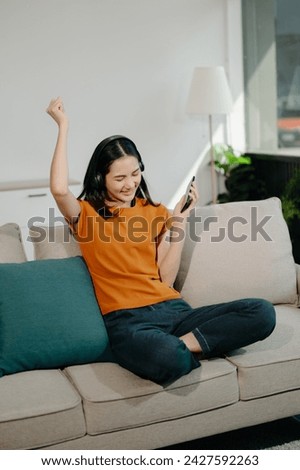 Young asian woman using smartphone and tablet while seated on couch on sofa at home
