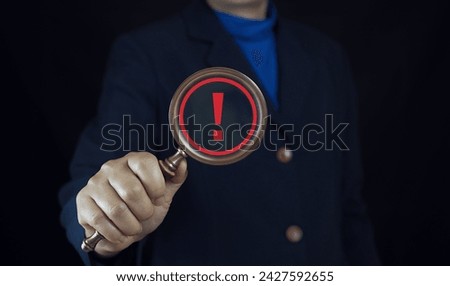 Businessman holding magnifier glass with red triangle caution warning sign for notification error and maintenance concept.
