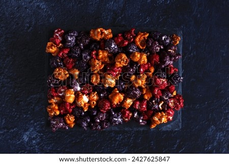 Multi-colored popcorn in caramel glaze on a board on a dark background