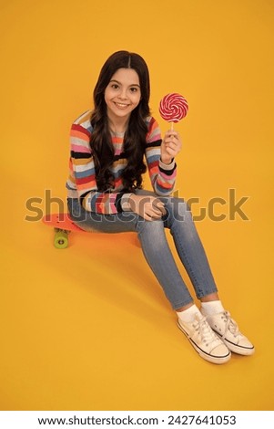 Hipster teenager child girl lick lollypop. Sugar nutrition, candy and sweets. Child eat lollipop popsicle. Happy teenager, positive and smiling emotions of teen girl.