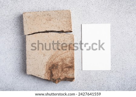 Blank paper sheet card and natural stone on gray concrete background. Mockup scene for design.