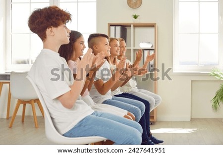 Group of children applauding after presentation in class or at school event. Side profile view of happy student boys and girls sitting in audience, looking away, clapping hands and smiling
