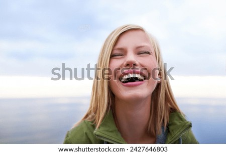 Woman, excited and happy at the beach for holiday, vacation and travel in winter. Face of a young person in the USA laughing and smile by an ocean, sea or lake with cloudy sky for outdoor adventure