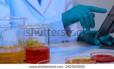 Scientists are doing research in a science lab. A medical chemist in a white coat, gloves and goggles looks at a glass tube. Compare two different liquid samples. and discuss future experiments.