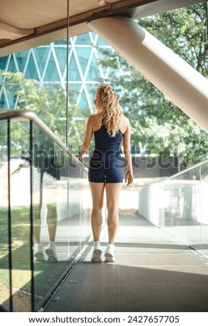 Back view of the sportive blonde woman standing at the street during the warm summer day after making exercises. Stock photo