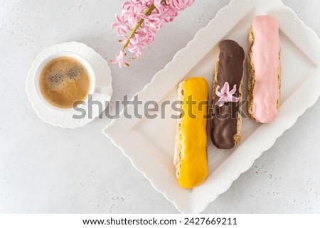 Delightful eclairs banner. Set of colorful eclairs, a cup of coffee and spring hyacinth flower on white background. Bakery banner, cafe advertisement, confectionery special offer. Top view, copy space Royalty-Free Stock Photo #2427669211