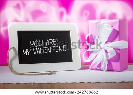 Image of a slate blackboard with chalk message YOU ARE MY VALENTINE and pink gift