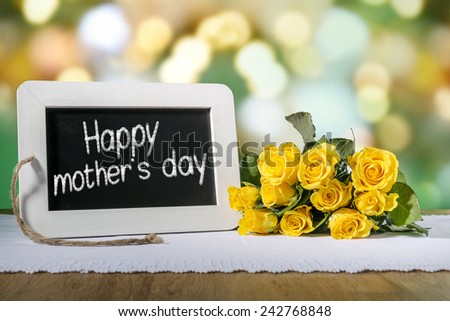 Image of a slate blackboard with message Happy mothers day on a wooden table with yellow roses