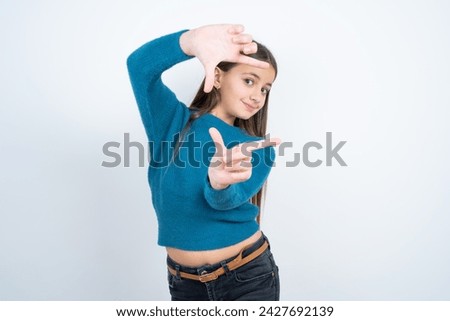 beautiful kid girl wearing blue t-shirt over white background making finger frame with hands. Creativity and photography concept.