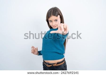 beautiful kid girl wearing blue t-shirt over white background making fun of people with fingers on forehead doing loser gesture mocking and insulting.