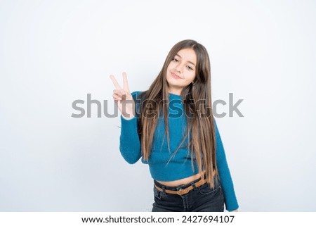 beautiful kid girl wearing blue t-shirt over white background smiling with happy face winking at the camera doing victory sign. Number two.