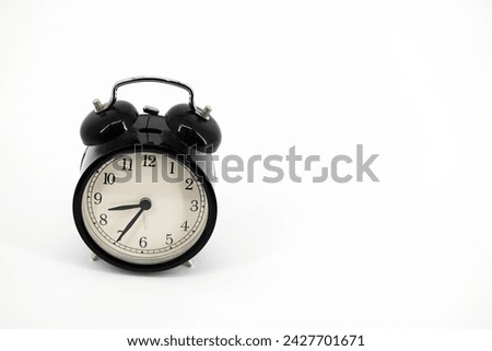 
A black alarm clock featuring two bells on top, chrome handle, and legs, captured against a pristine white background.  Royalty-Free Stock Photo #2427701671
