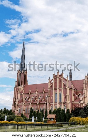 church building facade, arch, frescoes, stained glass windows against a background of green trees and a clear blue sky with clouds in summer and spring