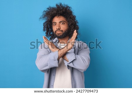 Young confident attractive Arabian man demonstrates prohibitory gesture to stop interlocutor words or express civil position about political system of country stands on blue background.