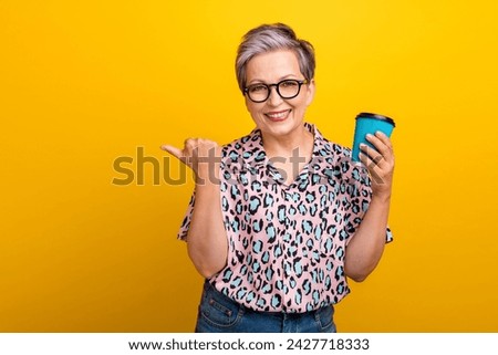 Photo of attractive pensioner woman hold paper cup point empty space wear trendy leopard print clothes isolated on yellow color background