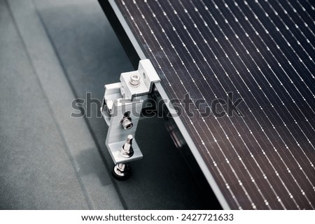Close up of solar panel, securely fastened with robust mounting clamp to supporting structure on rooftop of house. Bolts and clamps provide stability and durability to solar installation. Royalty-Free Stock Photo #2427721633