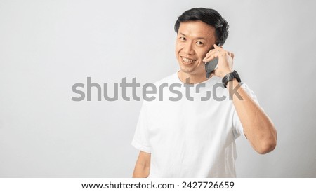 Portrait of an Indonesian Asian man, wearing a white T-shirt, talking on his smartphone, isolated against a white background.