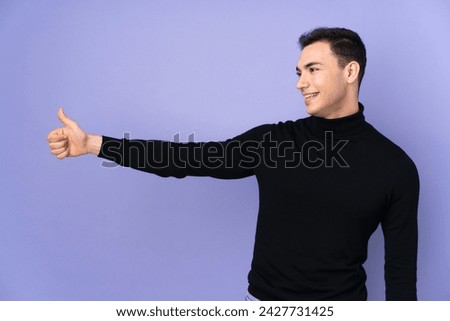 Young caucasian handsome man with turtleneck sweater isolated on purple background giving a thumbs up gesture