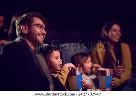 A modern family enjoys quality time together at the cinema, indulging in popcorn while watching a movie with their children Royalty-Free Stock Photo #2427732949