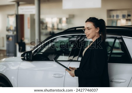Saleswoman with clipboard near car in dealership. High quality photo