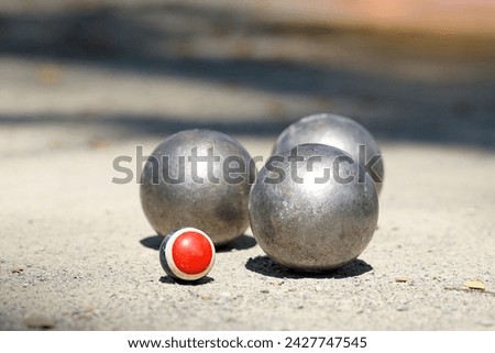 Petanque balls are placed near a target ball on an outdoor dirt field, where 12 round metal balls are thrown as close as possible to the target team that reaches 13. The first to score is the winner. 