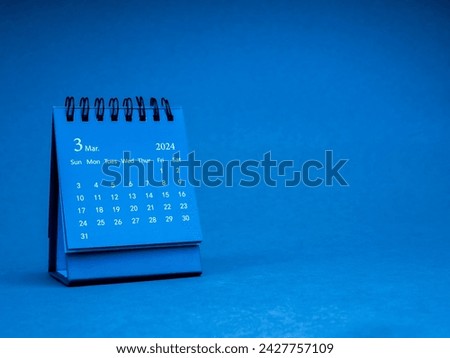 The March 2024, blue small spiral desk calendar for organizer to plan and reminder isolated on blue paper background with copy space, minimal style. Small table calendar with the page of third month.