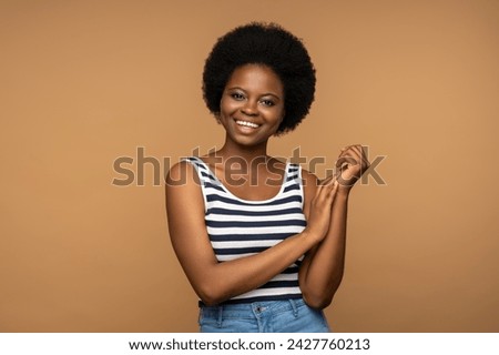 Positive cheerful young black woman with natural curly hair, looking at camera, smiling charismatically. Dark skinned female of african ethnic nationality posing for picture on studio background