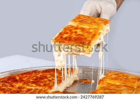Turkish traditional pastry with cheese, su boregi. A hand holding a slice of cheesy pastry isolated on white background. Royalty-Free Stock Photo #2427769287