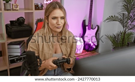 Vivacious young, blonde woman gamer seriously conquers virtual worlds playing video games, streaming her indoor gaming room night escapades with a laugh Royalty-Free Stock Photo #2427770013