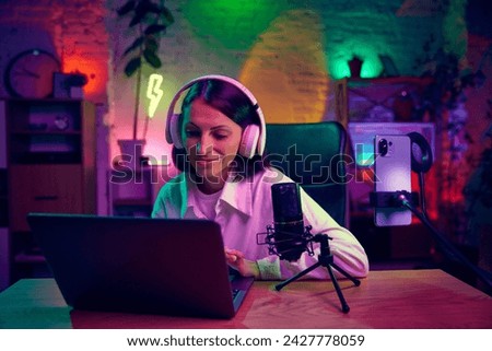 Young woman, blogger, streamer in headphones, sitting at home in modern room and leading online stream, podcast. Blogging, online services, streaming, education concept