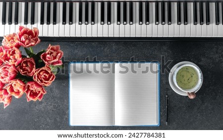 Piano, bouquet of spring flowers, notepad and cup of tea on a dark background.